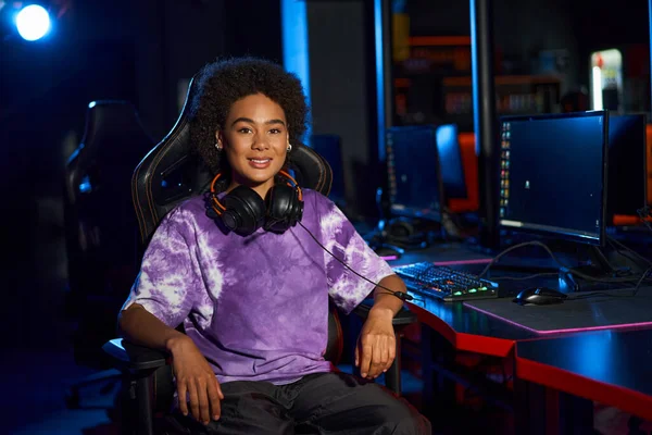 Happy african american female gamer with headphones sitting on comfortable gaming chair, cybersport — Stock Photo