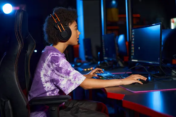 Lockige Afroamerikanerin mit Kopfhörer, die Computerspiel spielt, während sie auf den Bildschirm schaut, Cybersport — Stockfoto