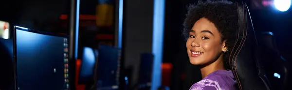 Весела афроамериканка сидить в ігровому кріслі і дивиться на камеру, кіберспорт банер — стокове фото