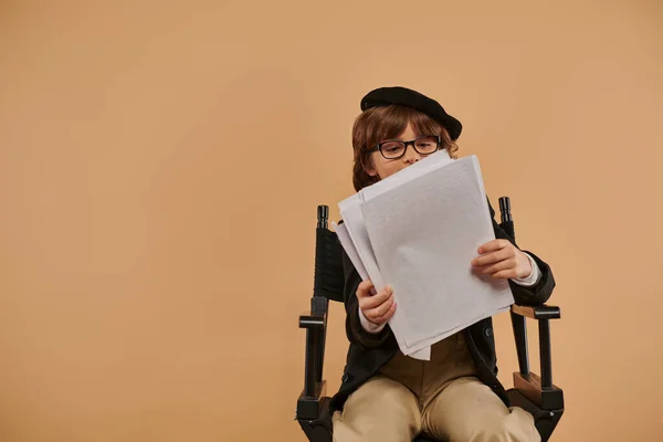 Occupato ragazzo in bicchieri si siede in sedia regista, guardando le carte e assorbito nella sua lettura — Foto stock