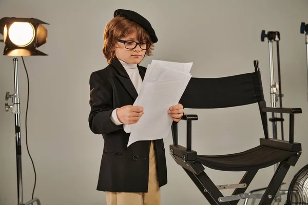 Хорошо одетый ребенок в очках и берете с собой сценарий на бумаге, мальчик в качестве режиссера — стоковое фото