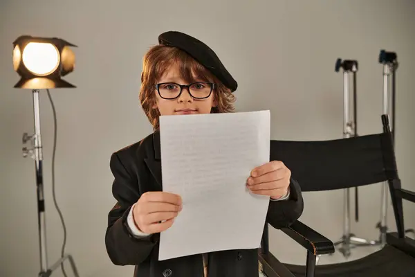 Хорошо одетый ребенок в очках и берет чтение сценария на бумаге, мальчик в качестве режиссера — стоковое фото