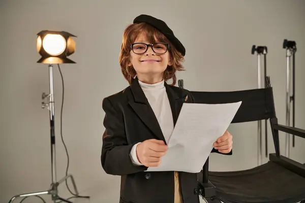 Bambino allegro in occhiali e basco che legge la sceneggiatura su carte, ragazzo come regista del regista — Foto stock