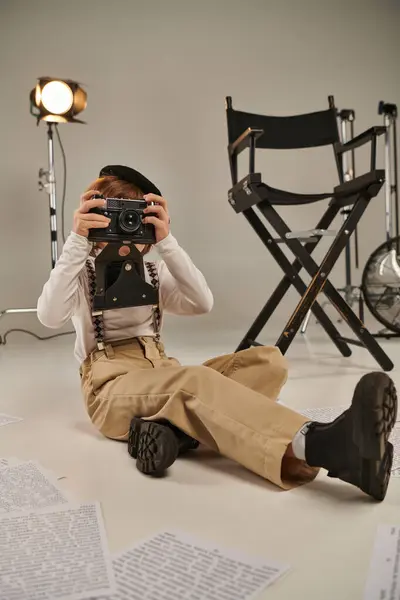 Niño captura el momento en la cámara mientras está sentado rodeado de guion y silla de director - foto de stock