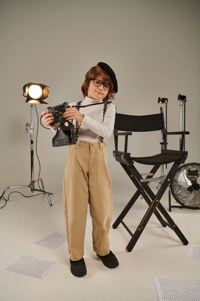 Boy in beret and glasses captures the moment on retro camera near director chair, young photographer — Stock Photo