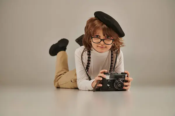 Jeune photographe en béret et lunettes prenant des photos à la caméra et couché sur le sol, garçon créatif — Photo de stock