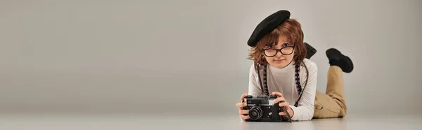 Boy photographer in beret and glasses taking photo on camera and lying on floor, banner — Stock Photo