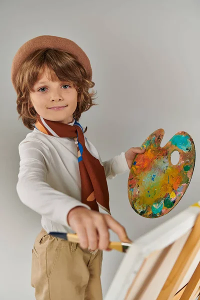 Хлопчик досліджує свій творчий потенціал, щасливого художника в Береті з барвистим розписом палітри біля мольберта — стокове фото