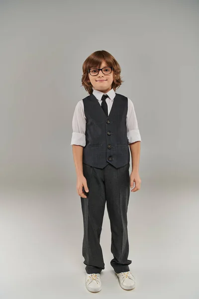 Future businessman, happy boy in elegant formal attire and glasses standing on grey background — Stock Photo