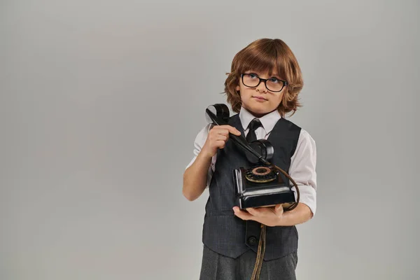 Élégant garçon dans des lunettes et gilet élégant tenant téléphone rétro sur fond gris, nostalgie — Photo de stock