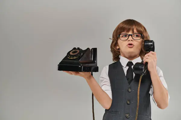 Netter Junge mit Brille und eleganter Weste, der am Retro-Telefon auf grauem Hintergrund spricht, Nostalgie — Stockfoto