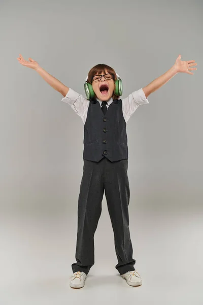Menino alegre cantando como levantar os braços em triunfo enquanto ouve música através de seus fones de ouvido — Fotografia de Stock