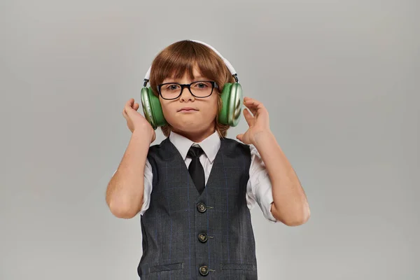 Menino elegante em óculos e traje elegante com colete ouvir música através de seus fones de ouvido — Fotografia de Stock