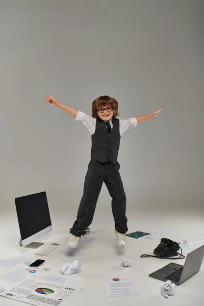 Niño alegre levitando cerca de dispositivos y suministros de oficina, profesionalidad y determinación - foto de stock