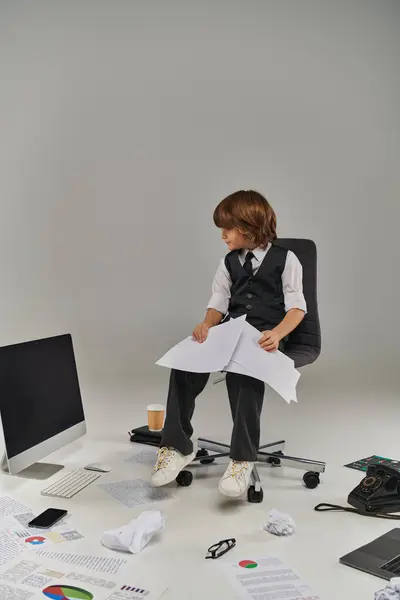 Menino em traje formal revisa documentos cercados por material de escritório, futuro profissional — Fotografia de Stock