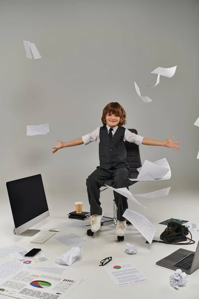 Menino feliz em traje formal sentado perto de documentos em ar e material de escritório, futuro profissional — Fotografia de Stock