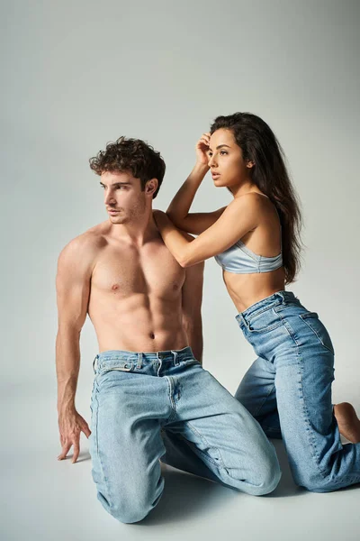 Sensual young woman in satin bra and jeans posing with shirtless man on grey background, closeness — Stock Photo
