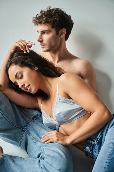 Brunette jeune femme en satin soutien-gorge appuyé sur sexy homme torse nu en jeans sur fond gris — Photo de stock