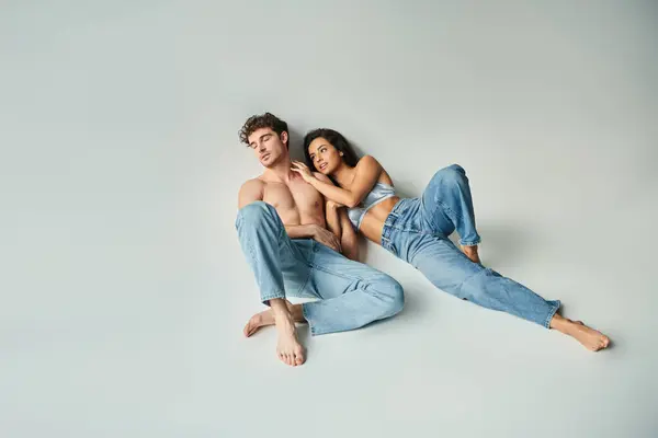 Sexy jovem mulher no seda sutiã inclinado no bonito sem camisa homem no azul jeans no cinza fundo — Fotografia de Stock