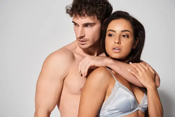 Sexy und hemdlos Mann umarmt verführerische junge und hübsche Frau auf grauem Hintergrund, Zweisamkeit — Stockfoto