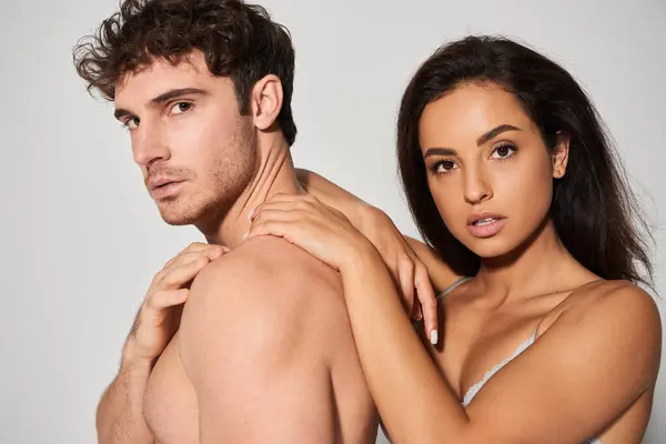 Seductive young woman with brunette hair leaning on shirtless man on grey background, models — Stock Photo