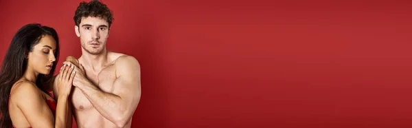 Homme musclé regardant caméra près de magnifique femme brune en soutien-gorge sur fond rouge, bannière — Photo de stock