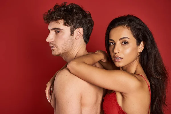 Magnifique et brune femme en soutien-gorge appuyé sur beau copain torse nu sur fond rouge — Photo de stock