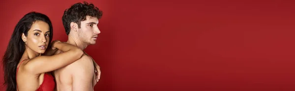 Magnifique et brune femme en soutien-gorge appuyé sur beau copain torse nu sur fond rouge, bannière — Photo de stock