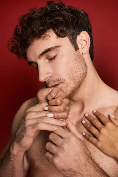 Bel homme beau et torse nu embrassant les mains de sa petite amie sur fond rouge, affection — Photo de stock