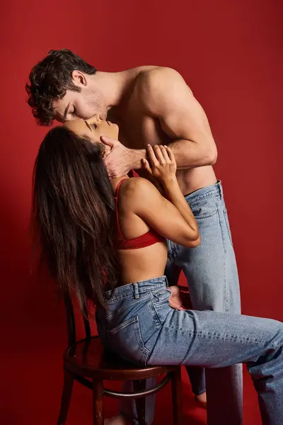 Hombre sin camisa y musculoso con los ojos cerrados besar joven morena mujer sobre fondo rojo - foto de stock