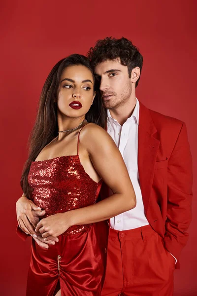 Elegant young couple in evening attire hugging during romantic date on Valentines day, red backdrop — Stock Photo