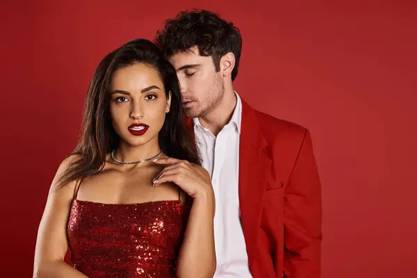 Handsome man in formal wear seducing beautiful young woman in shiny dress on red background — Stock Photo