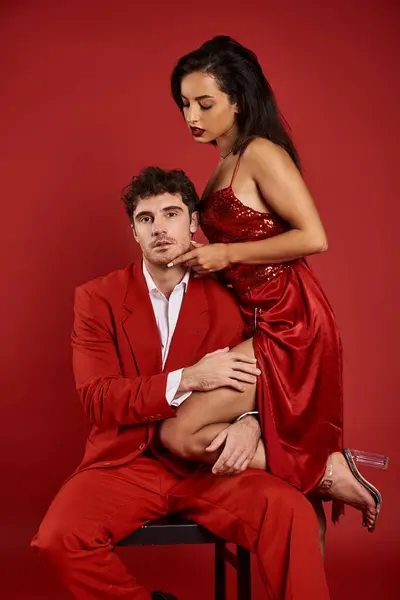 Витончена молода жінка в сексуальній сукні спокушає красивого чоловіка в офіційному одязі на червоному тлі — стокове фото