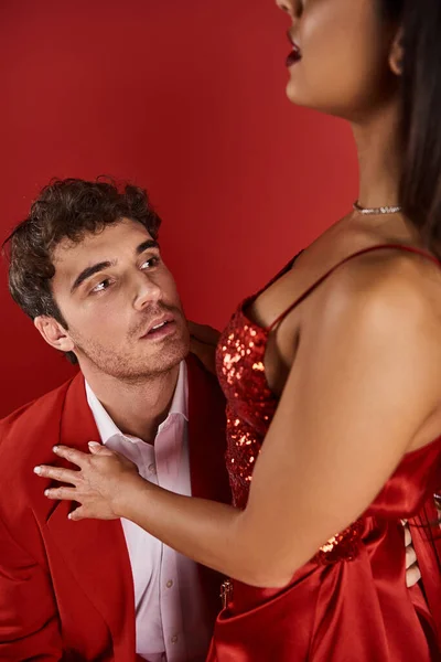 Красивий чоловік у формальному одязі, дивлячись на елегантну молоду жінку в сукні на червоному тлі, прихильність — стокове фото