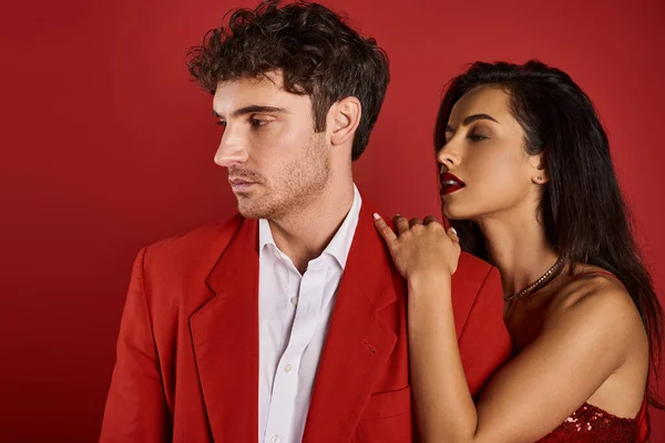 Sophistiqué jeune femme avec des lèvres rouges séduire bel homme en tenue formelle sur fond rouge — Photo de stock