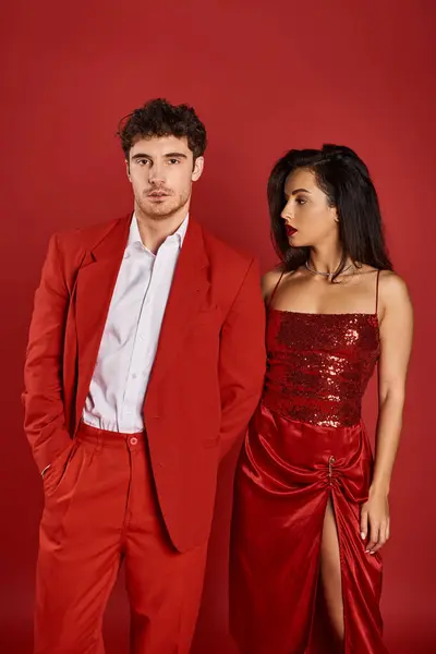 Élégante jeune femme aux lèvres rouges séduisant bel homme posant sur fond rouge, main dans la poche — Photo de stock