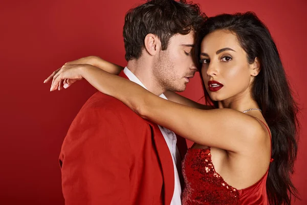 Sophisticated and brunette young woman in elegant dress embracing handsome man on red background — Stock Photo