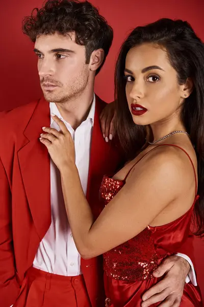 Jeune femme brune avec des lèvres rouges embrassant bel homme en tenue formelle sur fond rouge — Photo de stock