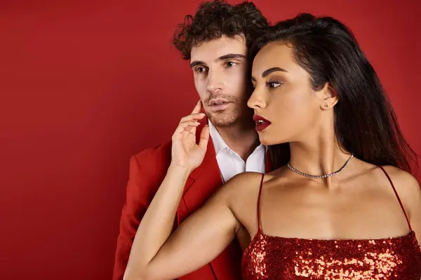 Jeune femme attrayante avec des lèvres rouges posant près de bel homme en tenue formelle sur fond rouge — Photo de stock