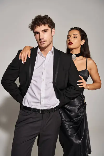 Attractive young woman with red lips embracing handsome man in suit on grey background, passion — Stock Photo