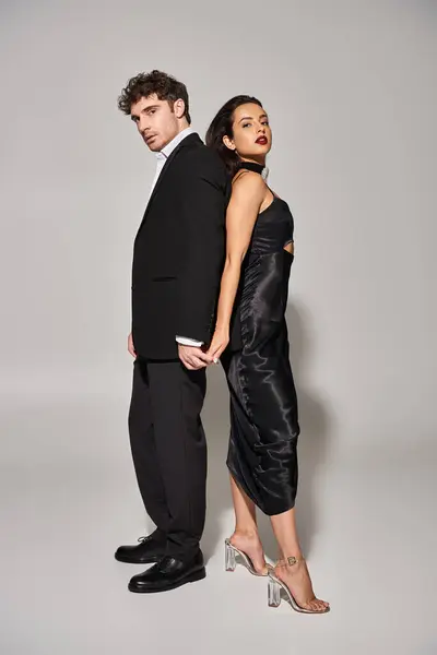 Longitud completa de la elegante pareja en traje de noche de pie juntos sobre fondo gris, glamour - foto de stock