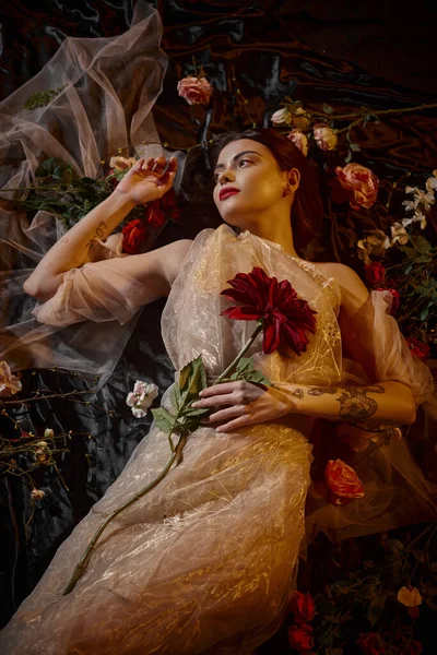 Feminine elegance, pierced young woman in romantic transparent dress lying among beautiful flowers — Stock Photo