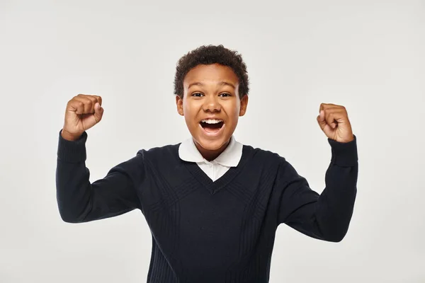 Excited african american schoolboy in uniform rejoicing while looking at camera on grey backdrop — Stock Photo