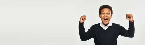 Animado afro-americano estudante em uniforme regozijo enquanto olha para a câmera em cinza, banner — Fotografia de Stock