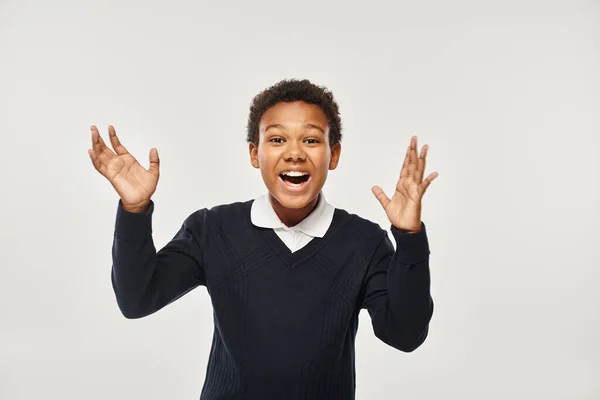 Excité afro-américain garçon en uniforme scolaire se réjouissant tout en regardant la caméra sur fond gris — Photo de stock