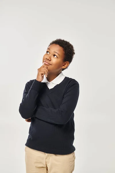 Pensive african american boy in school uniform touching chin while thinking on grey backdrop — Stock Photo