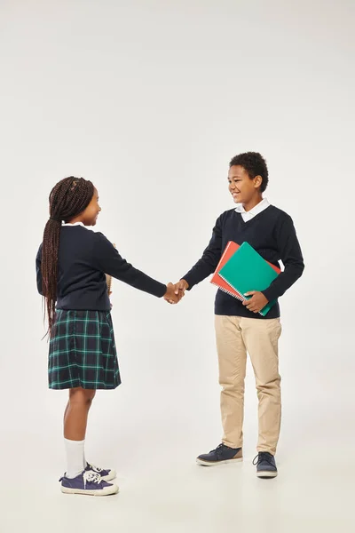 Щасливі афроамериканські діти в шкільній формі тримають підручники і тремтять руками на сірому тлі — стокове фото