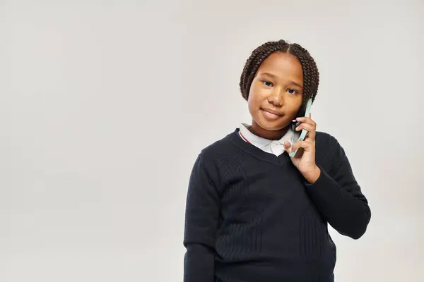 Preteen african american schoolgirl in uniform talking on smartphone on grey background, phone call — Stock Photo