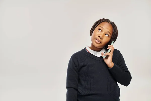 Preteen african american schoolgirl in uniform talking on smartphone on grey background, look away — Stock Photo