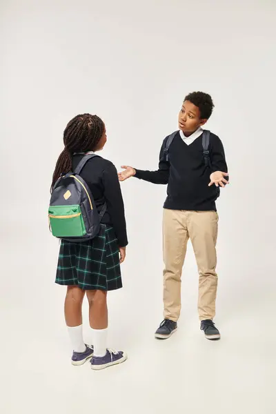 Афроамериканські школярі з рюкзаками, що стоять разом і спілкуються на сірому фоні — стокове фото